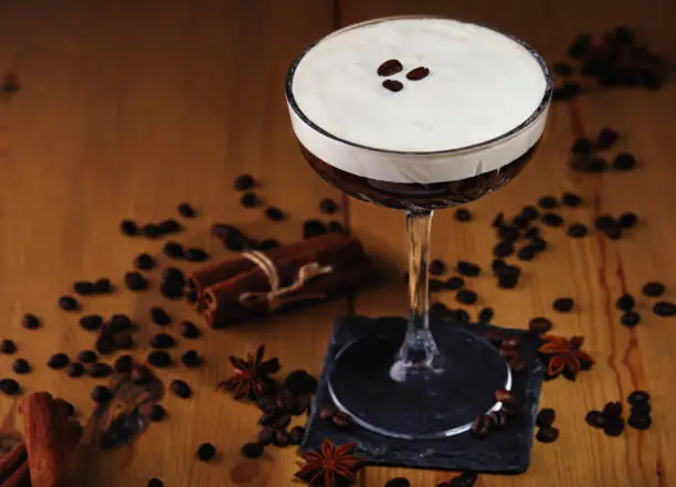 Photo of Espresso martini cocktail in a glass with coffee grains, cinnamon and star anise on a wooden background