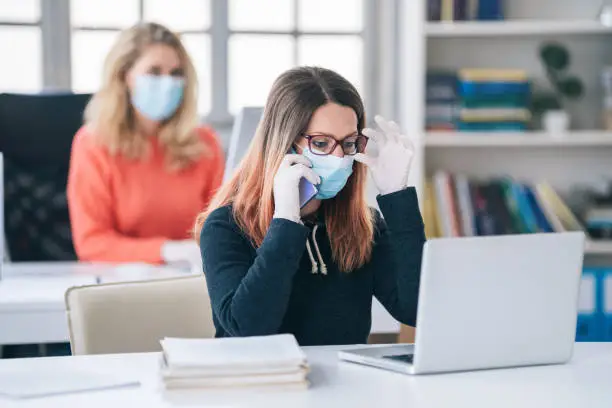 Photo of Colleagues in the office working while wearing medical face mask during COVID-19