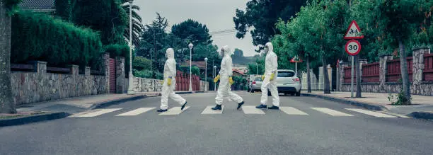 Group of people in bacteriological protection suits crossing a crosswalk on an empty street