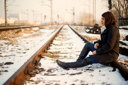A sad young woman is sitting on the railroad tracks