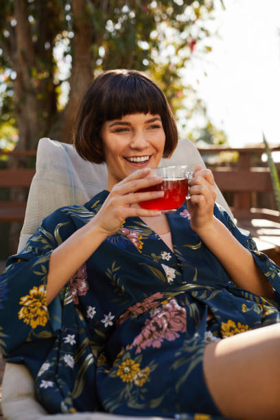 istock Young woman in a robe laughing and drinking tea on her patio 1213508355