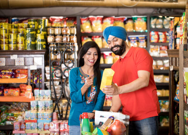 Couple shopping at supermarket Happy Indian couple reading product information while shopping at grocery store convenience store stock pictures, royalty-free photos & images