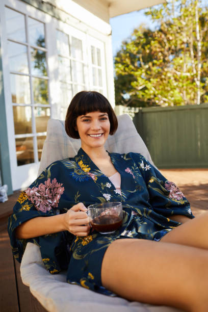 istock Smiling young woman lying on a deck chair and drinking tea 1213510150