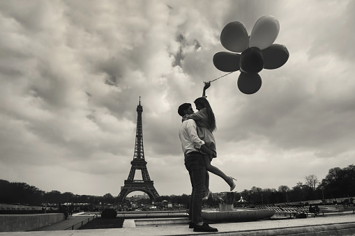 vintage photo of Paris with affectionate couple holding balloons near Eiffel tower, retro style view