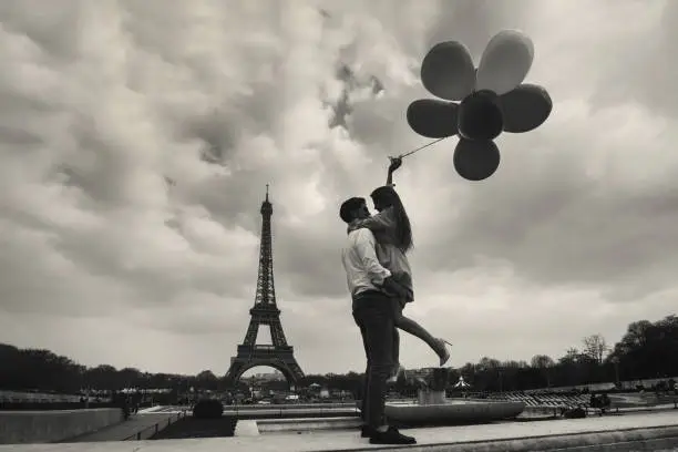 Photo of vintage photo of Paris with affectionate couple holding balloons near Eiffel tower, retro style