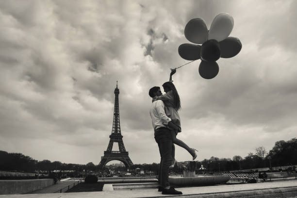 vintage photo of paris with affectionate couple holding balloons near eiffel tower, retro style - paris france eiffel tower love kissing imagens e fotografias de stock