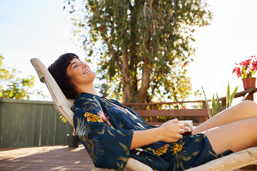 Laughing young woman wearing a robe and relaxing on a deck chair outside on a sunny afternoon