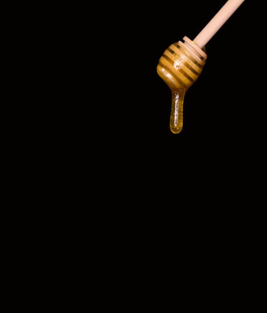 istock Sugar paste or beauty wax for sugaring flows from a wooden dipper. Black background, free space for text. Honey drips from the spoon. 1213513154