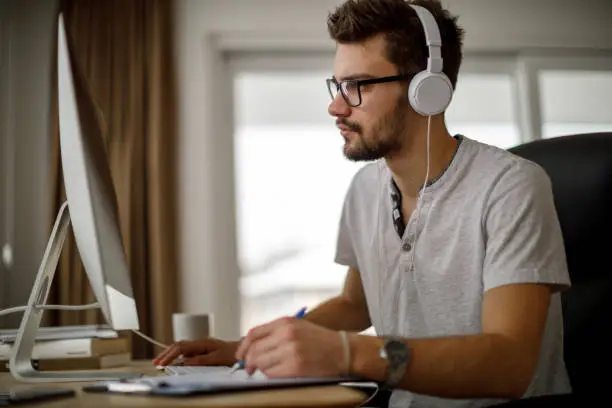 Photo of Young man using computer and taking notes