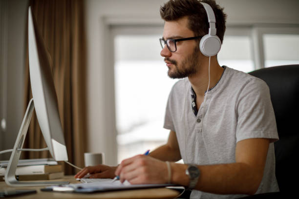 jovem usando computador e tomando notas - development research business workshop - fotografias e filmes do acervo