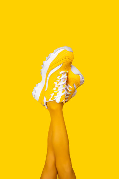 Yellow female sneakers on long woman legs isolated on yellow background. Vertical banner. New Yellow female sneakers on long woman legs in yellow tights isolated on yellow background. Monochrome pop art concept. Vertical banner yellow shoes stock pictures, royalty-free photos & images