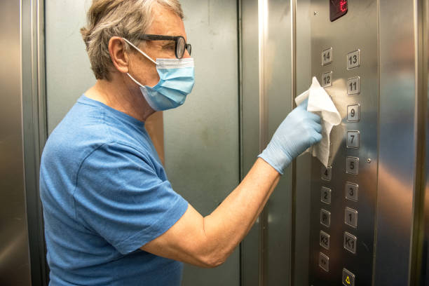 Senior Man Wiping Down the Inside of the Elevator for Covid-19, Europe Senior man wiping down the elevator buttons, Slovenia, Europe. Nikon D850. hand elevator stock pictures, royalty-free photos & images