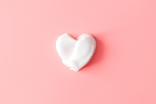 Heart from soap foam on pink background. White cleanser texture. Concept hygiene and healthcare