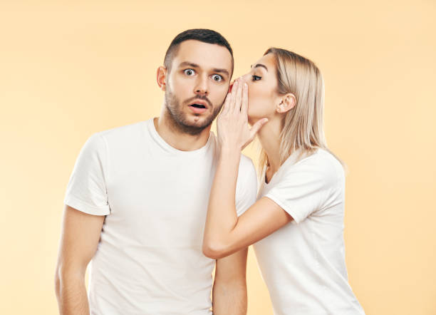 istock Young woman whispering secrets to man over beige background 1213524615