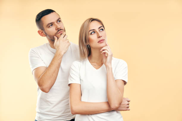 Young thoughtful man and woman looking sideways isolated on beige background Young thoughtful man and woman looking sideways isolated on beige background. Doubt, interest concept two people thinking stock pictures, royalty-free photos & images