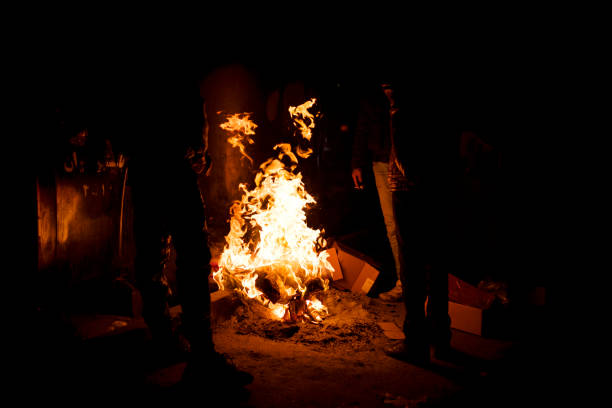 istock Three man have set a fire with garbages, papers, and cartons beside a garbage container. it's a cold night and they smoke and talk beside the fire. 1213525604