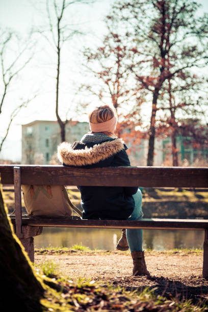 istock Enjoying the sun in spring: Young girl is sitting on park bench, back view 1213530963