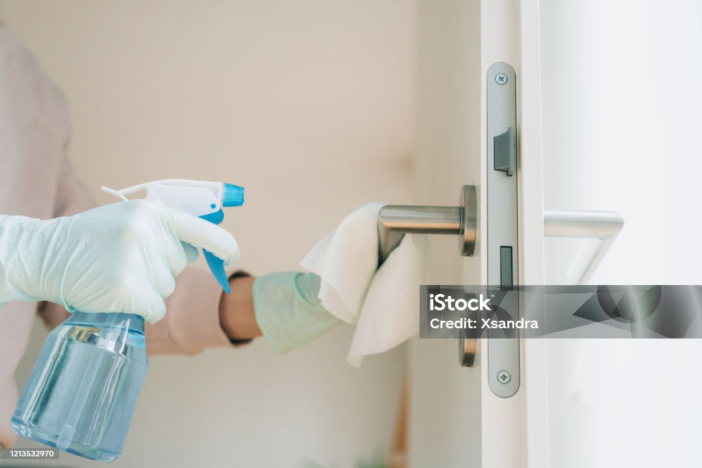 Woman cleaning a door handle with a disinfection spray Woman in protective gloves cleaning a door handle with a disinfection spray and disposable wipes Cleaning Stock Photo