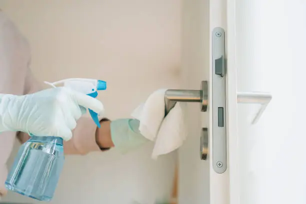 Woman in protective gloves cleaning a door handle with a disinfection spray and disposable wipes