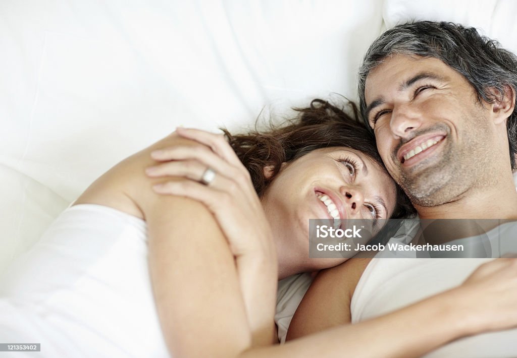 Cosy mature couple lying in bed smiling  Adult Stock Photo