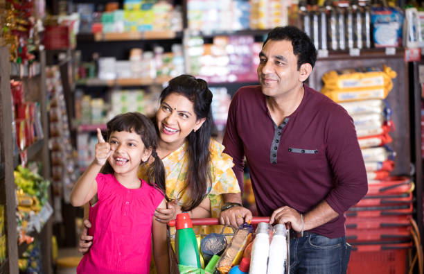 Happy family shopping for groceries at the supermarket Happy parents with daughter shopping for groceries at the supermarket while she points at something on shelf happy indian young family couple stock pictures, royalty-free photos & images