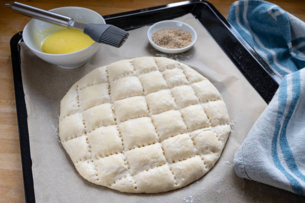istock Flat bread dough with the typical pattern for Turkish Ramadan pide on a baking tray with paper, egg yolk for coating and sesame seed 1213537717