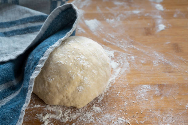 yeast dough for bread or cake will be covered with a kitchen towel to rest and rise on a wooden baking board, copy space - dough sphere kneading bread imagens e fotografias de stock