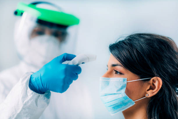 istock Coronavirus Screening. Medical worker in protective suit checking body temperature with contactless body thermometer, young woman wearing protective mask 1213540817