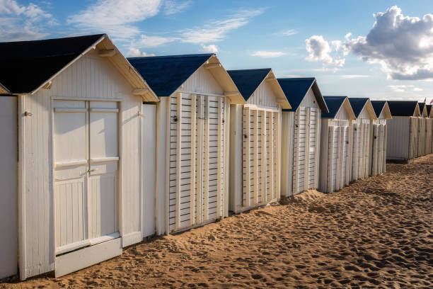 Row of white wooden beach huts or cabins alongside Riva Bella beach on early evening, Ouistreham, Normandy, France. stock photo