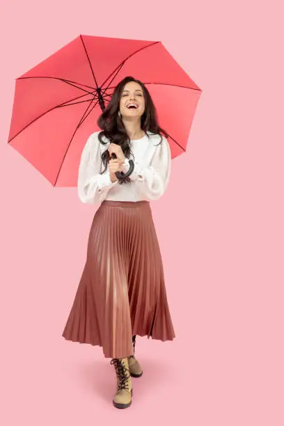 Photo of Young pretty dark-haired woman in a pleated skirt holding a red umbrella and smiling