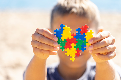 Boy hands holding colorful puzzle heart in front of his face. World autism awareness day concept.