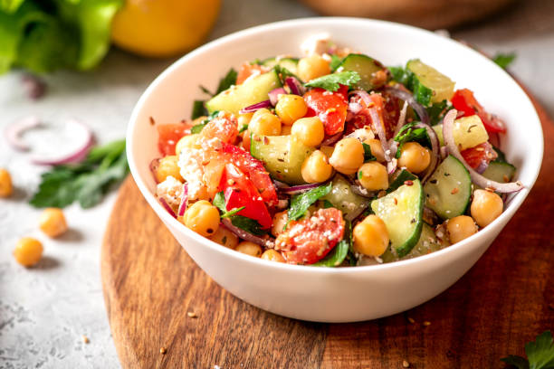 Chickpea salad in a plate on a served table Chickpea salad with tomatoes, cucumber, feta cheese, parsley, onions and lemon in a plate on a served table, selective focus. Tasty and healthy vegetarian food, oriental and Mediterranean cuisine. Salad stock pictures, royalty-free photos & images