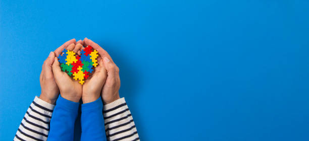世界自閉症啓発デーコンセプト。水色の背景にパズルの心を持つ大人と子供の手 - social awareness symbol 写真 ストックフォトと画像