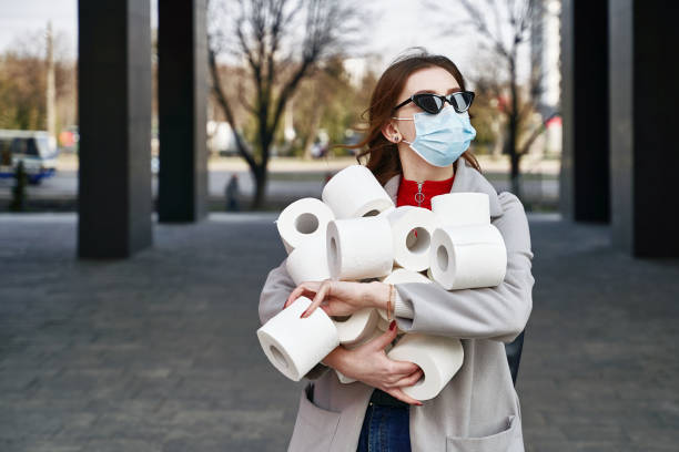 Young woman wearing protection face mask and sunglasses against coronavirus MERS-Cov, Novel coronavirus 2019-nCoV holds many rolls of toilet paper on the city street. Concept of coronavirus quarantine and pandemic. stock photo