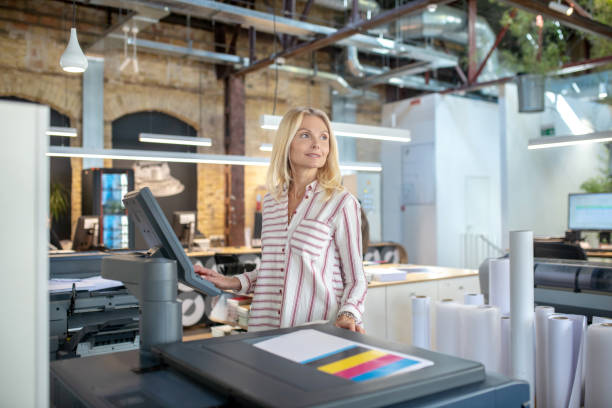 istock Blonde woman choosing paper printing settings, looking sideways 1213557067
