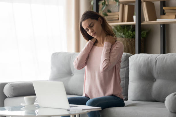 mulher cansada sentindo dor no pescoço após o trabalho de computador em casa - backache massaging pain back - fotografias e filmes do acervo