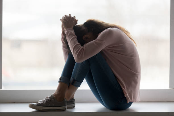 うつ病の悲しい十代の少女は家で泣いてシルに座る - mental health relationship difficulties teenager divorce ストックフォトと画像