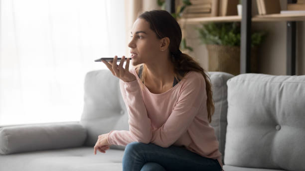 mujer joven sosteniendo el teléfono usando el reconocimiento de voz móvil en casa - personal data assistant fotografías e imágenes de stock