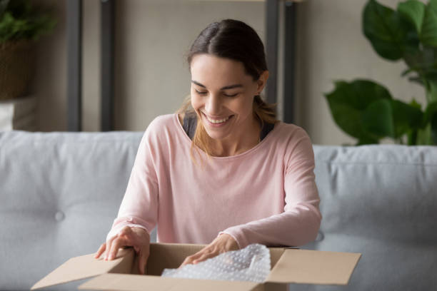 istock Smiling young woman customer open parcel cardboard box on sofa 1213557428
