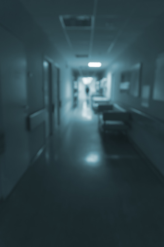 Dark blurred hospital corridor with a silhouette of a man in the background. Toned photo, out of focus