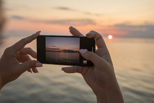 Young woman taking a picture of beautiful sunset