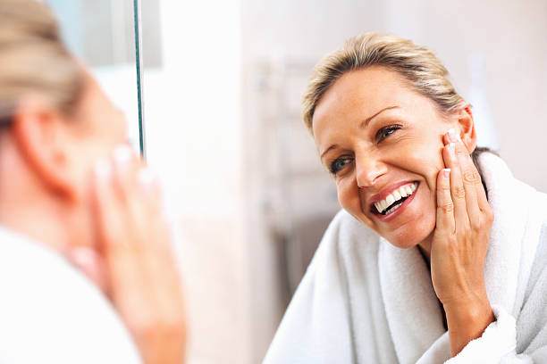 glückliche ältere frau genießen sie sich selbst im spiegel - hauptpflege stock-fotos und bilder
