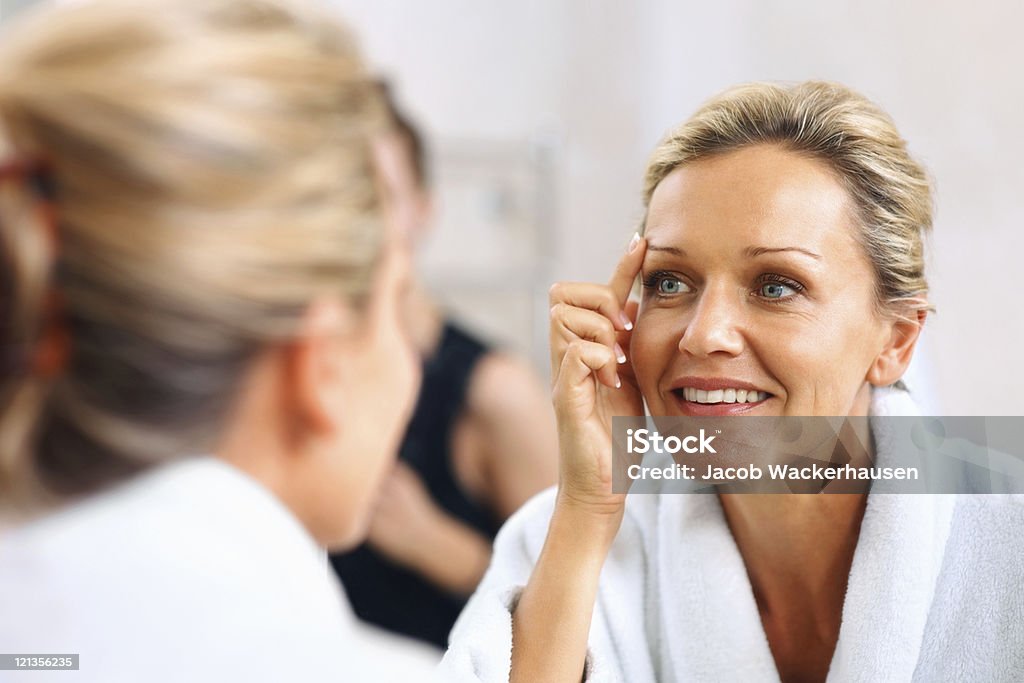 Hermosa mujer madura admira misma en el espejo - Foto de stock de Proceso de envejecimiento libre de derechos