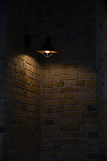 Night darkness and glowing retro style streetlight. Rough stone brick wall and metal lampshade. Architectural brickwork background with copy space. stock photo