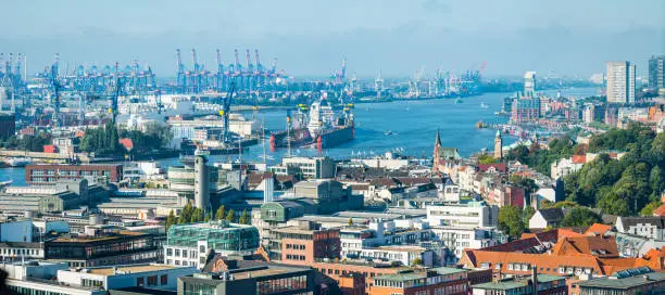 Panoramic aerial view over the rooftops of Hamburg to the busy cranes of the Port of Hamburg and blue waters of the Elbe, Germany.