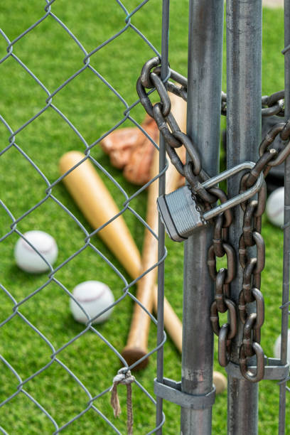 istock A chainlink fence gate that is locked with a padlock and baseball equipment 1213563907