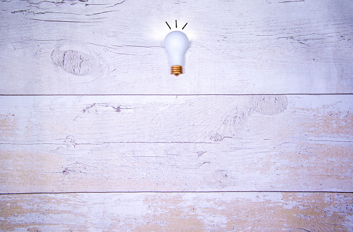 A single light bulb against a wood effect background. Giving the idea concept.