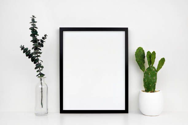 istock Mock up black portrait frame with cactus and branches on a white shelf 1213573708