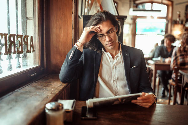 istock Serious businessman reading newspaper at local cafe 1213580417