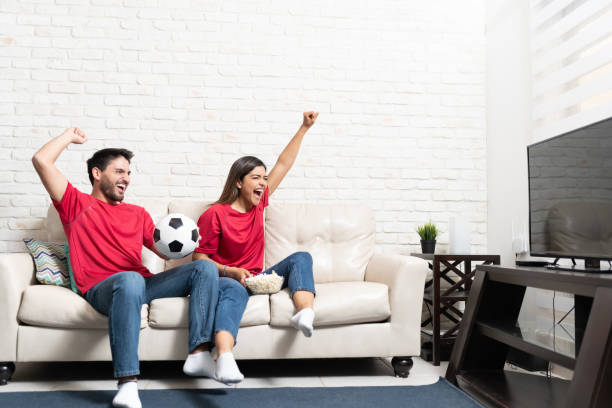 Couple Cheering While Watching Soccer Match On TV Cheerful Hispanic boyfriend and girlfriend watching soccer match on TV at home tv game stock pictures, royalty-free photos & images